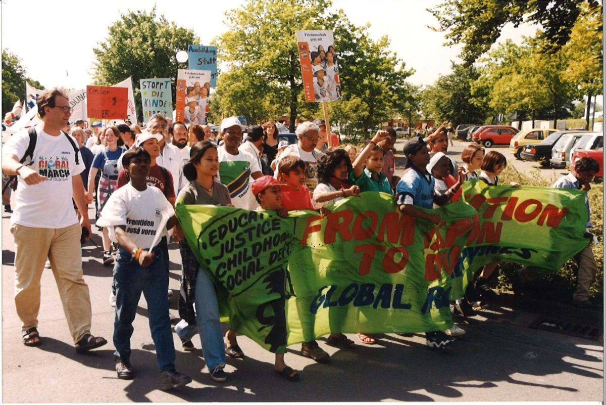 Demonstrationszug des Global March mit grünem Banner „From Education to Elimination